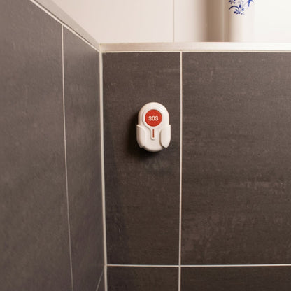 DigiWelzijn Aupero ovale waterbestendige SOS-alarmknop gemonteerd aan een grijze badkamertegelmuur